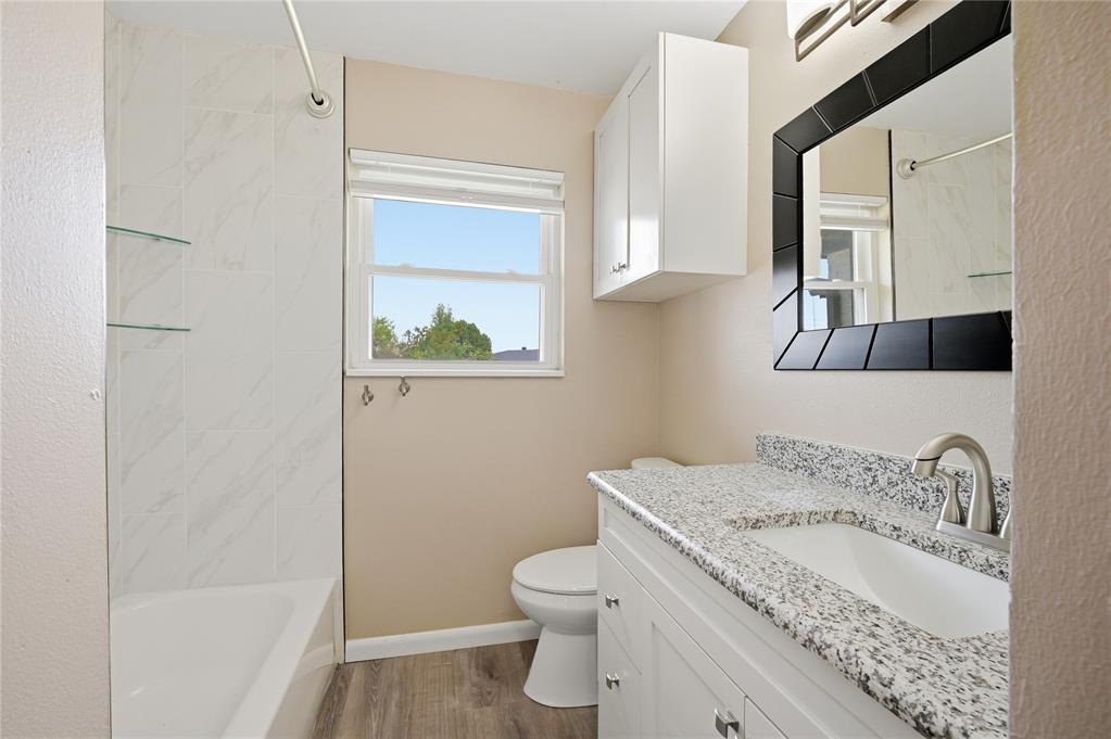 Bathroom with marble-look tub surround, window, and white vanity with speckled granite countertop.