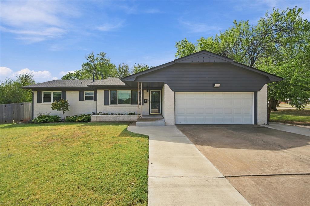 Single-story brick home with a dark gabled garage facade, concrete driveway, and green front lawn.