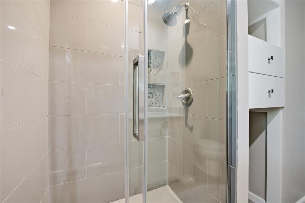 Glass-enclosed tiled shower with chrome fixtures and recessed wall niches.