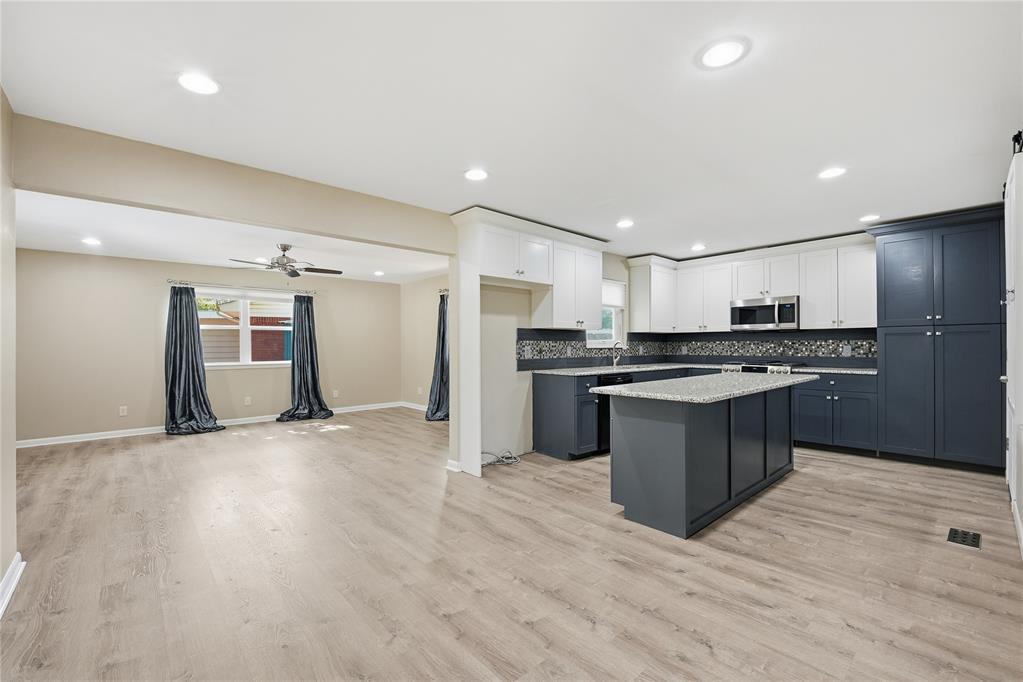 Open kitchen and living area with dark blue cabinets, granite island, and light wood-look floors.