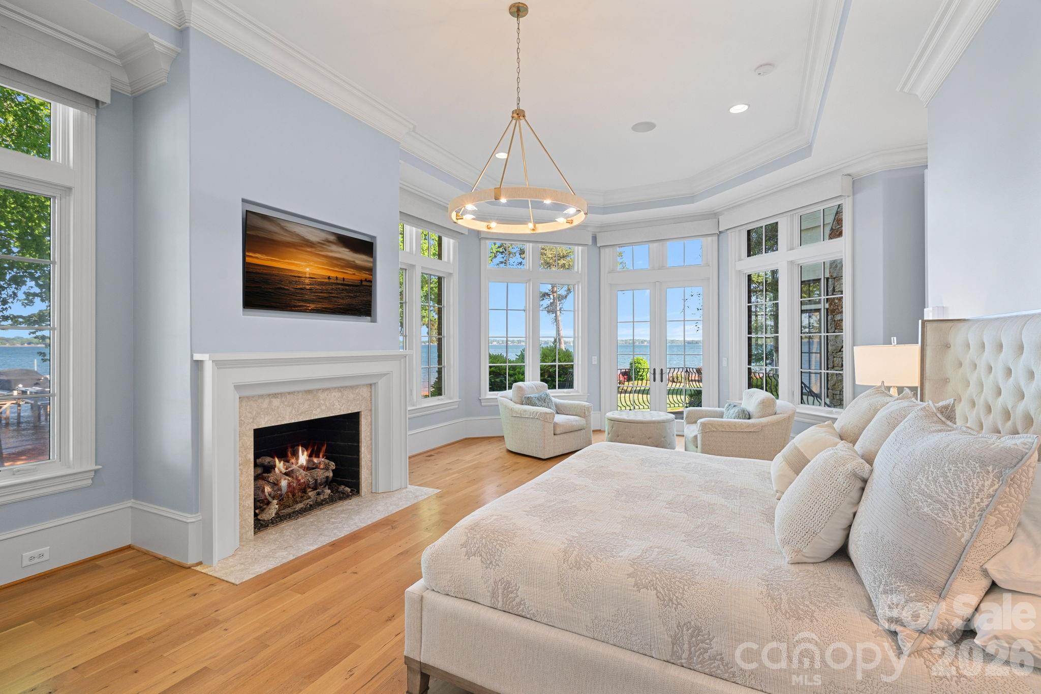 Waterfront bedroom with a fireplace, sitting area, and tall windows overlooking the lake.