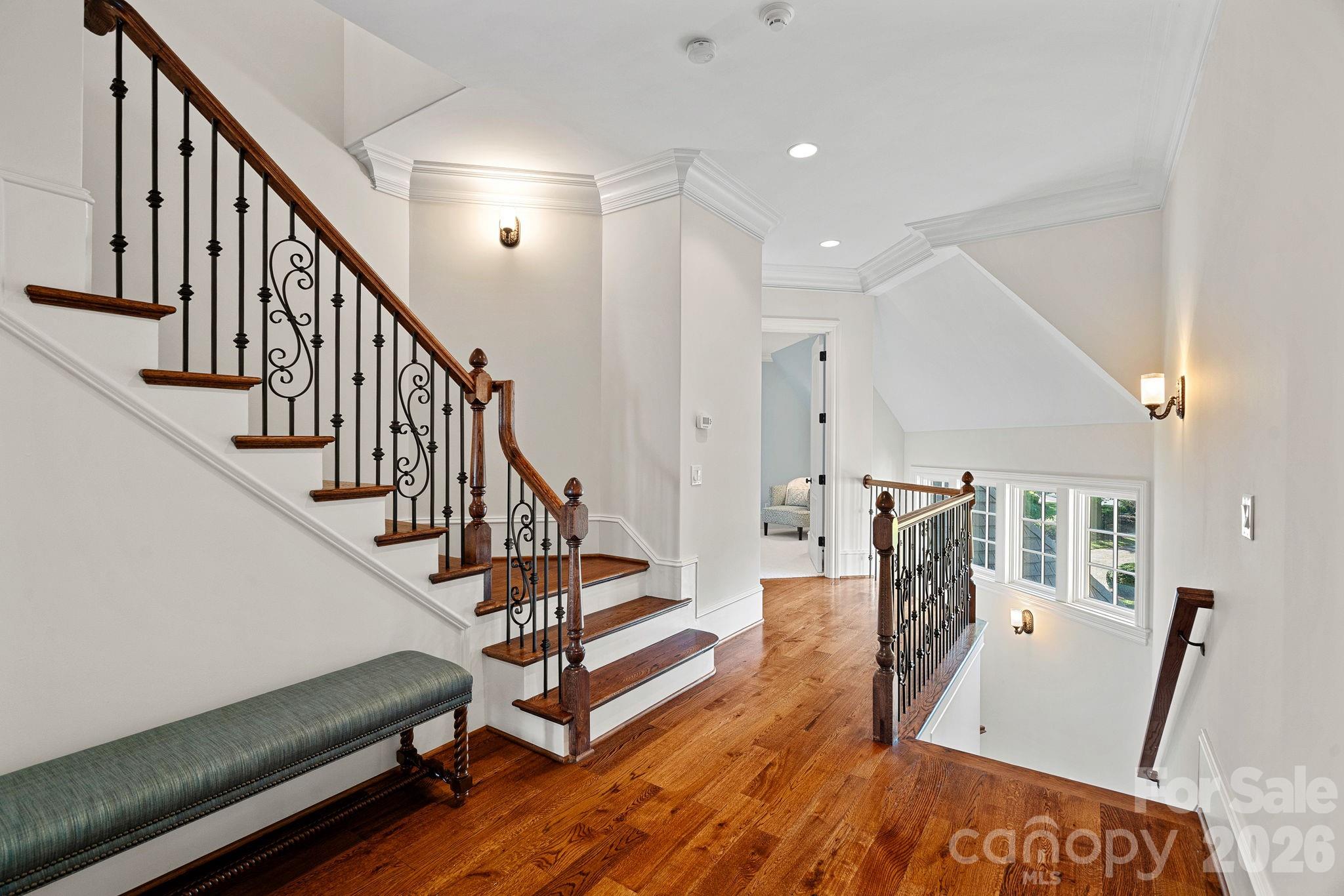 Two-story foyer with polished hardwood floors, an ornate wood-and-iron staircase, and a green upholstered bench.