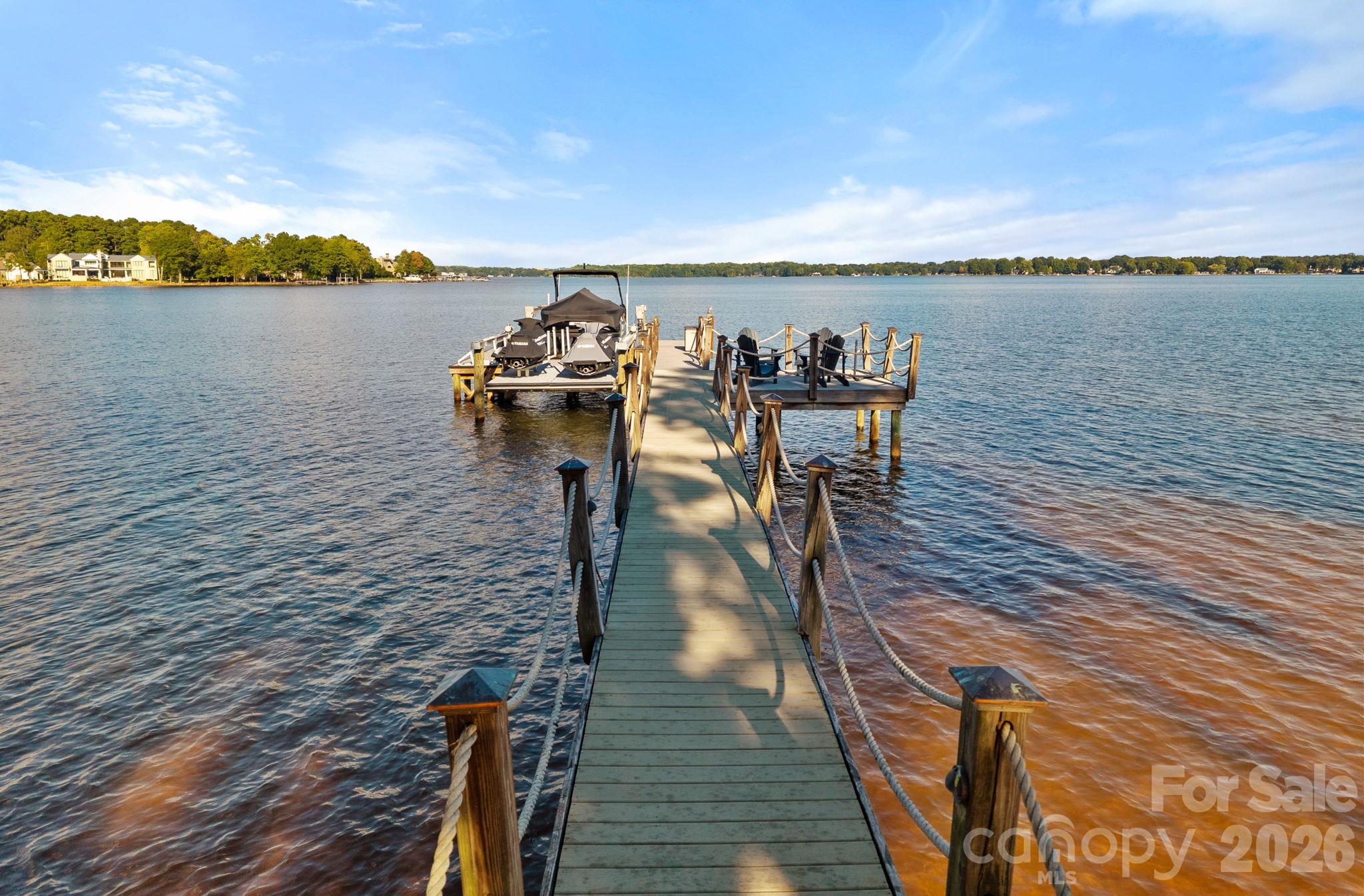 Lakefront dock with rope railings, covered boat slips, and a seating platform overlooking the water.