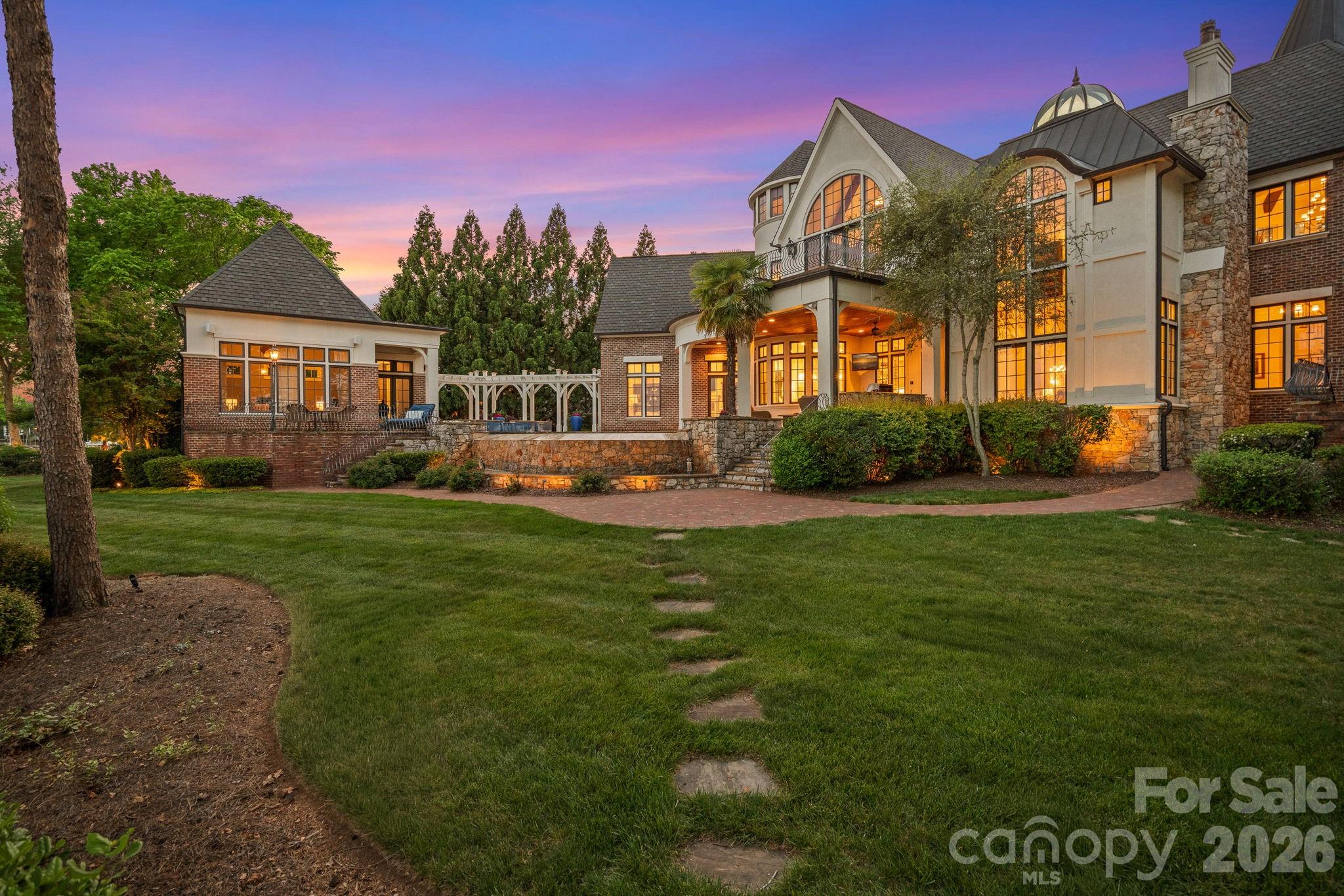 Large stone-and-brick home with a glass-domed turret and illuminated arched windows at dusk.