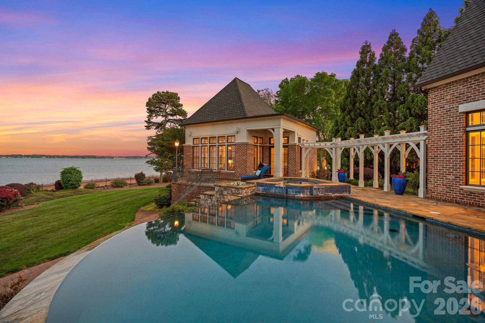 Waterfront home with a pool and covered patio overlooking the lake at sunset.