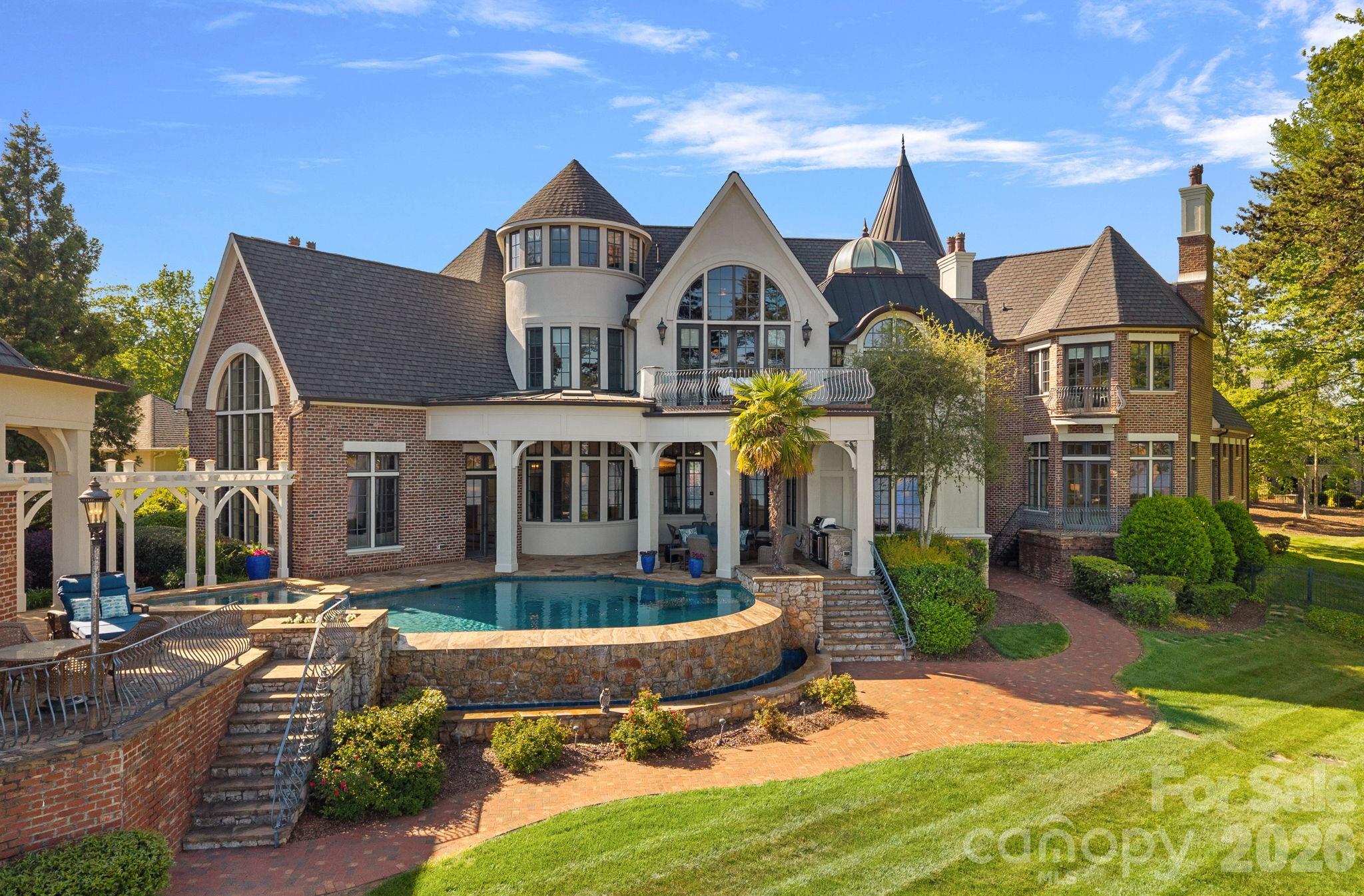 Large brick-and-stucco home with turreted roofs and a raised backyard swimming pool.