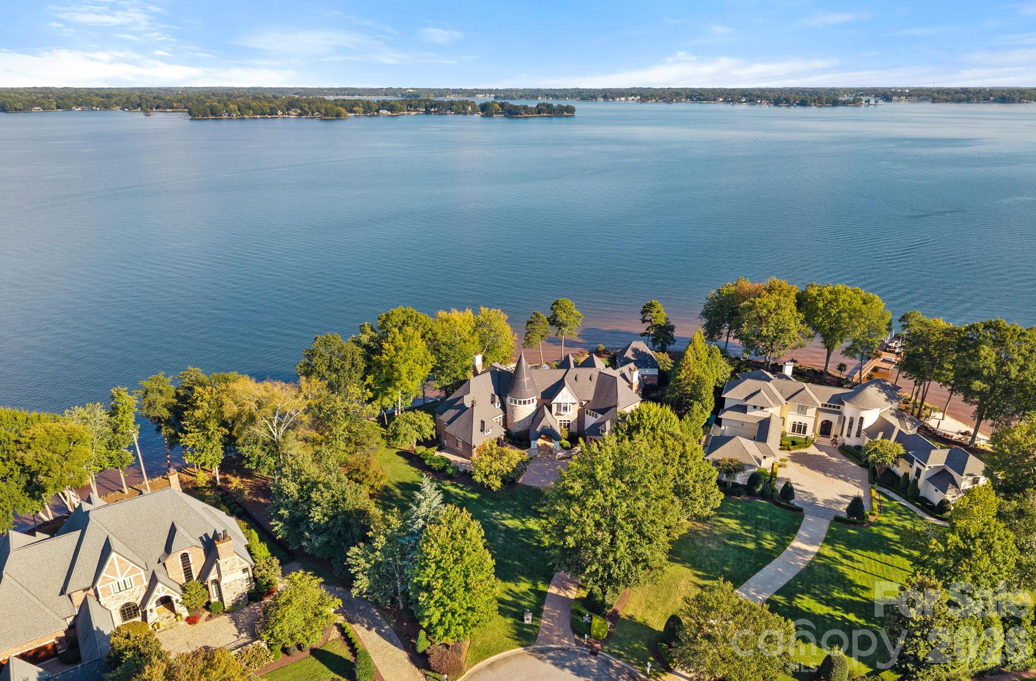 Aerial view of waterfront homes beside Lake Norman, with a stone house and turret among mature trees.