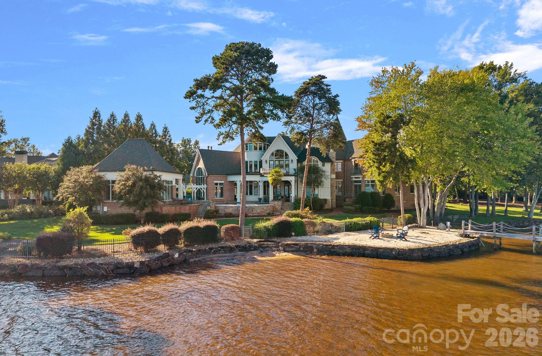 Waterfront home with arched windows, landscaped grounds, stone shoreline, and dock.