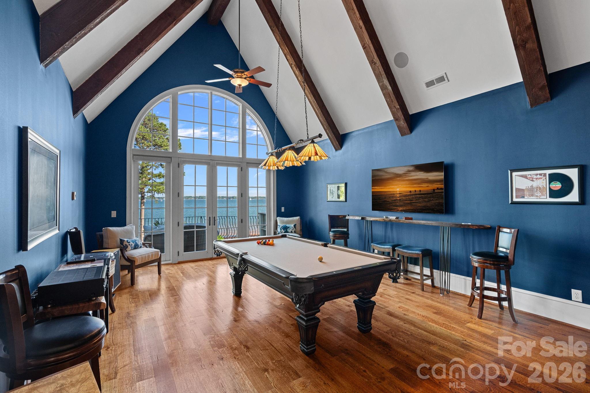 Game room with a pool table and arched windows overlooking the water.