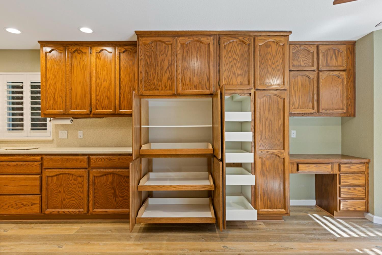 Kitchen with honey-oak cabinets, open pull-out pantry shelves, and a built-in desk area.