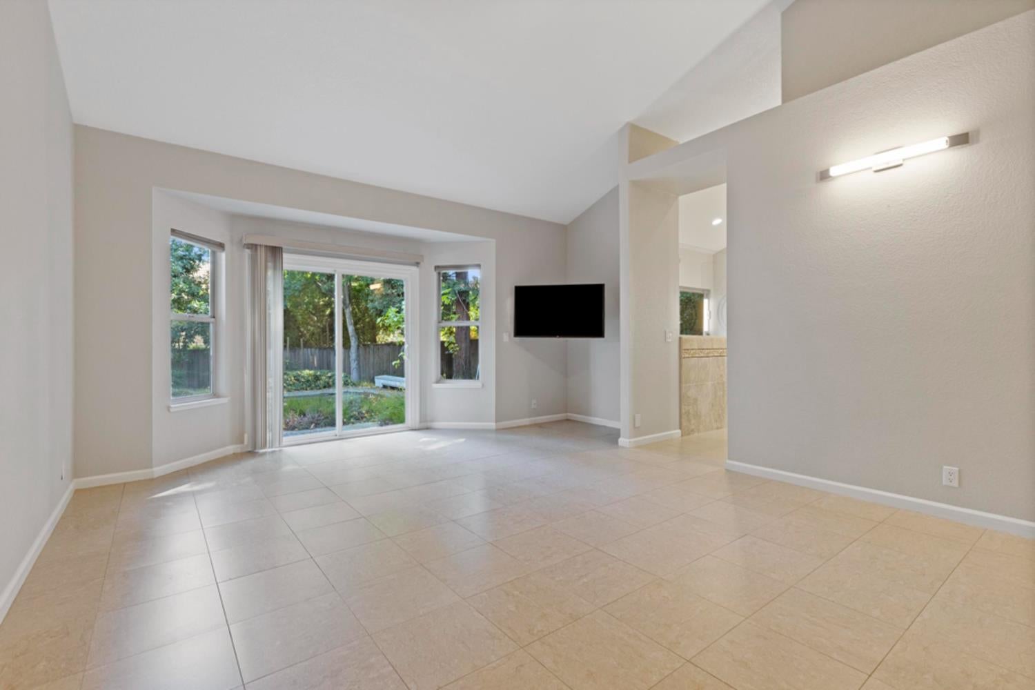 Unfurnished living room with beige tile floors, sliding glass doors, and a wall-mounted television.