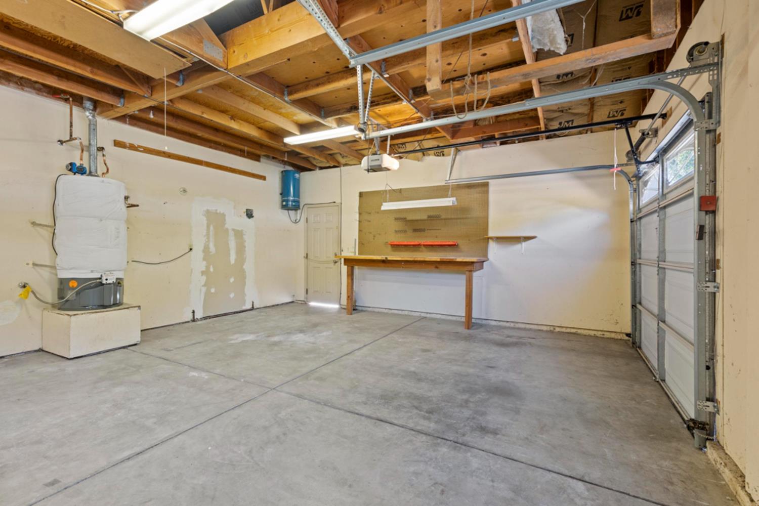 Empty garage with exposed ceiling framing, a workbench, water heater, and overhead garage door.