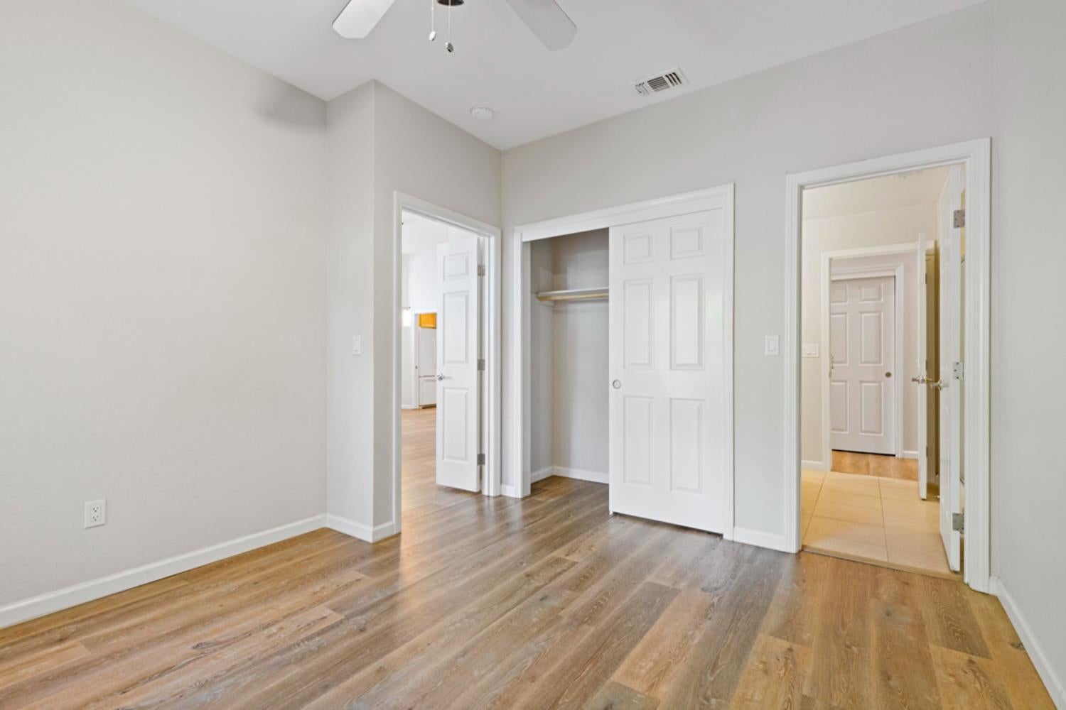 Empty bedroom with wood-look flooring, a ceiling fan, and an open closet.