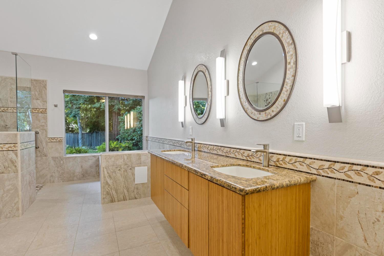 Bathroom with a long double vanity, two oval mirrors, patterned tile, and a window overlooking greenery.