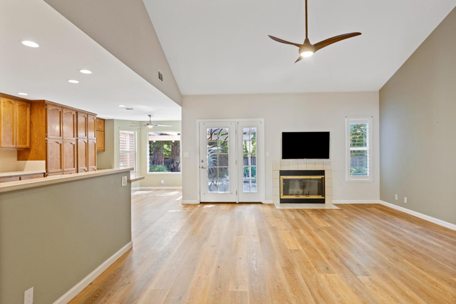 Empty living room with vaulted ceiling, wood floors, tiled fireplace, and glass French doors.