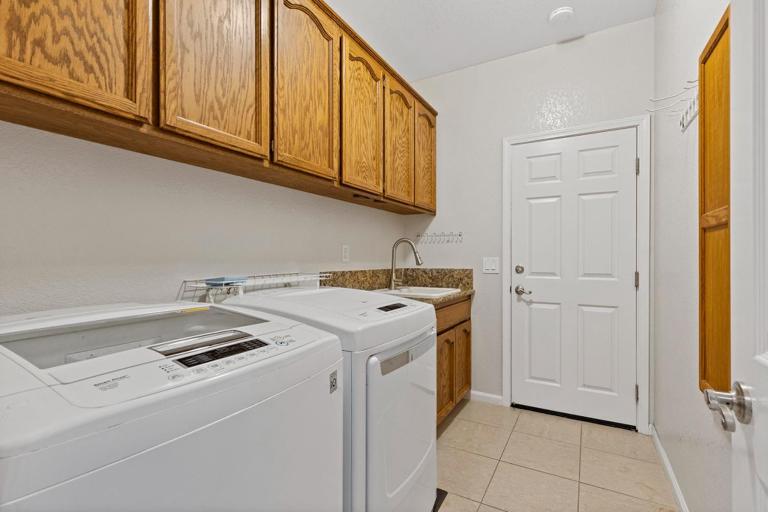 Laundry room with a washer and dryer, wood cabinets, and a utility sink.