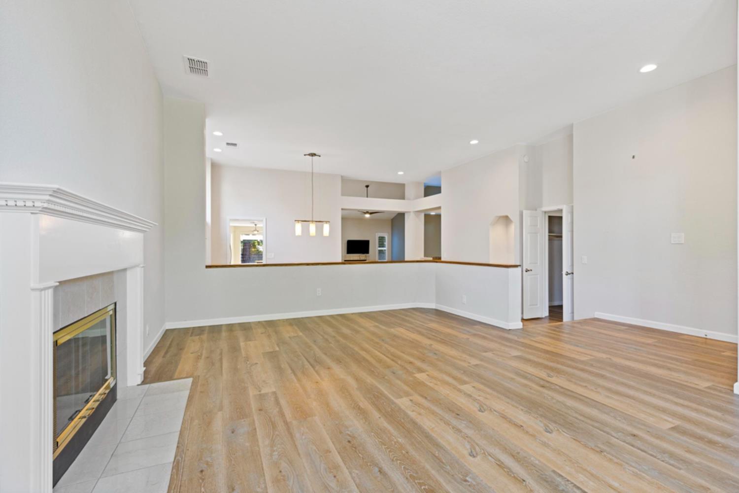 Empty living room with wood-look floors, a white fireplace, and high ceilings.