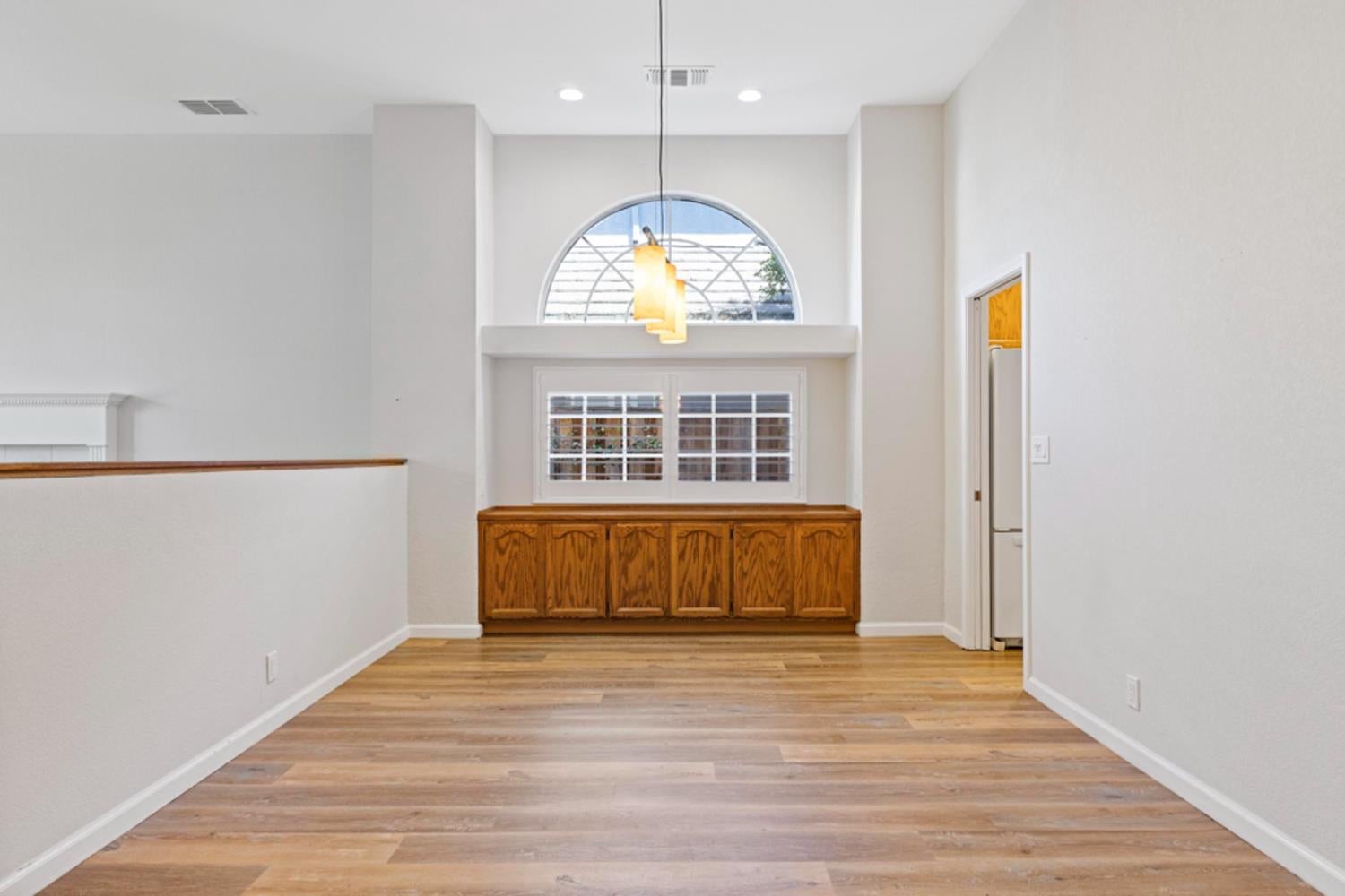 Vacant dining area with built-in oak cabinets, wood-look flooring, and a tall arched window.