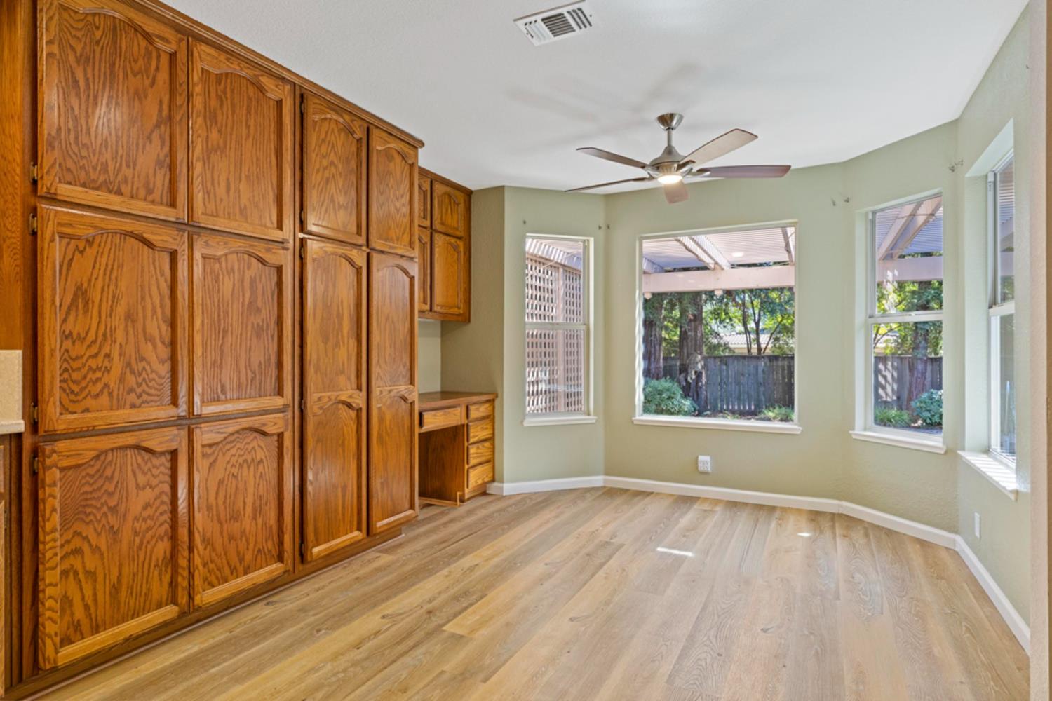 Empty bedroom with extensive oak built-in cabinets, light wood flooring, and windows overlooking a fenced yard.