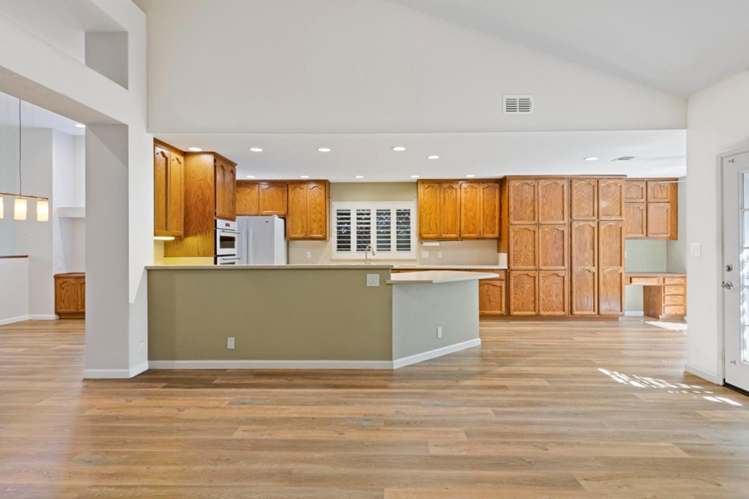 Open kitchen with honey-colored cabinets, a green-front peninsula, and light wood floors.