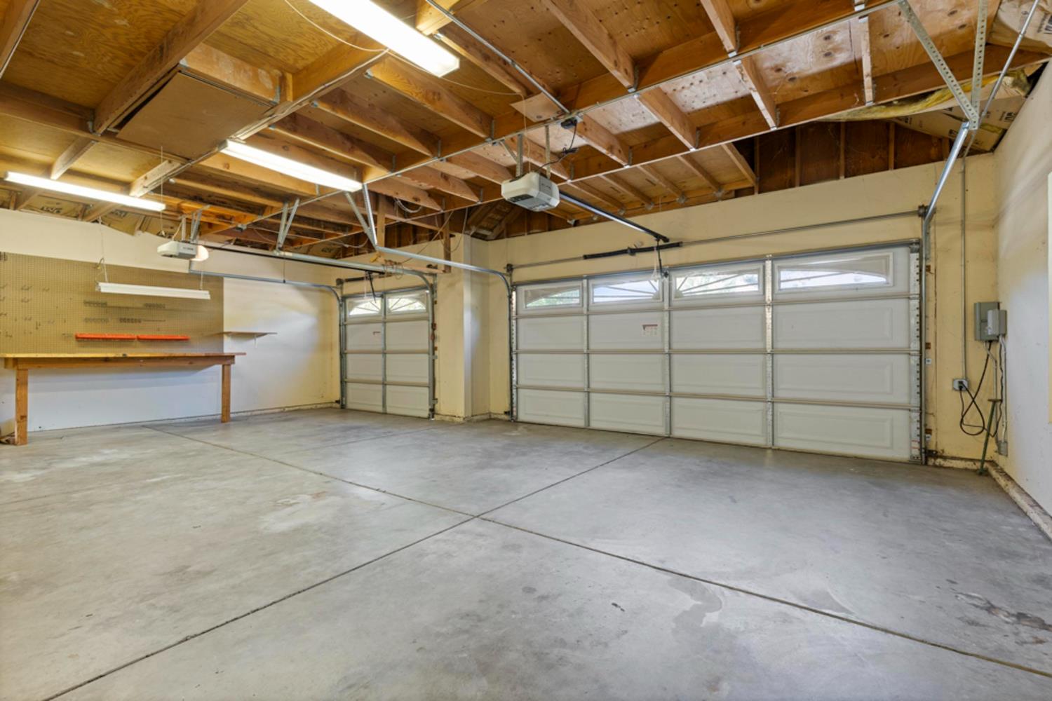 Empty garage with two doors, a concrete floor, exposed wood framing, and a built-in workbench.