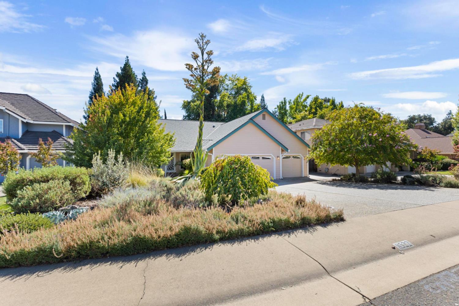 Home with teal-trimmed gables, a two-car garage, mature trees, and landscaped front beds.