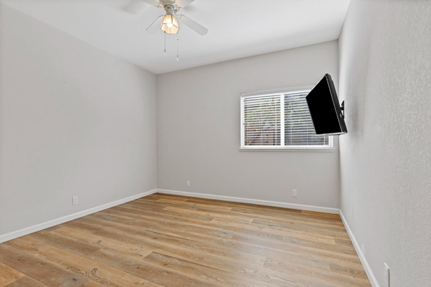 Empty bedroom with wood-look flooring, a ceiling fan, and a wall-mounted television.