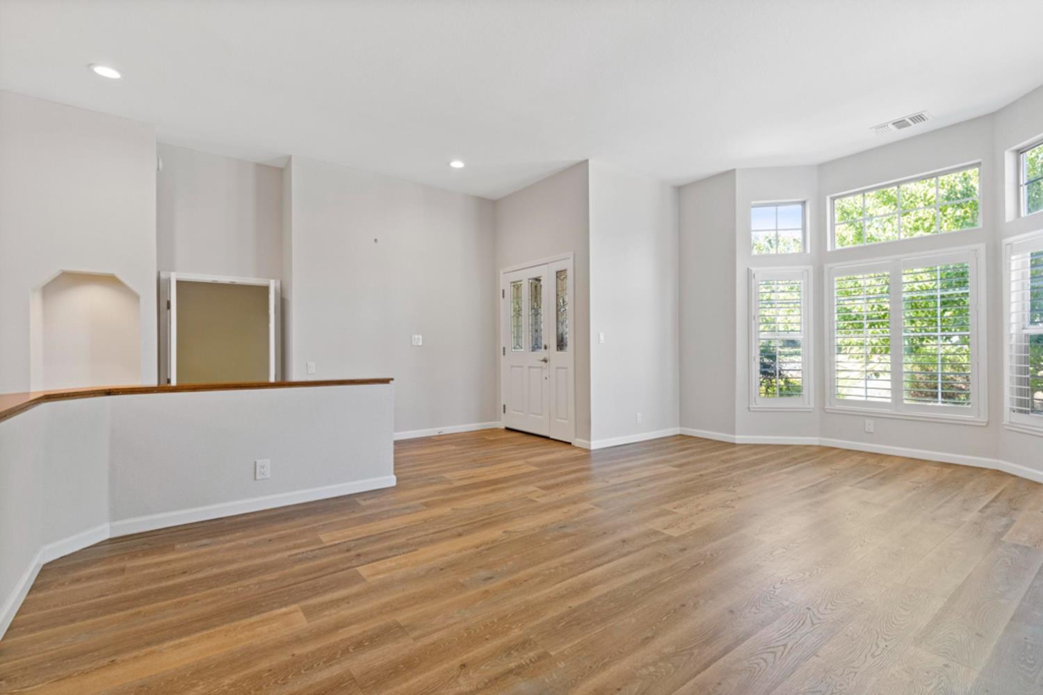 Vacant living room with wood floors, tall shuttered windows, and a high ceiling.