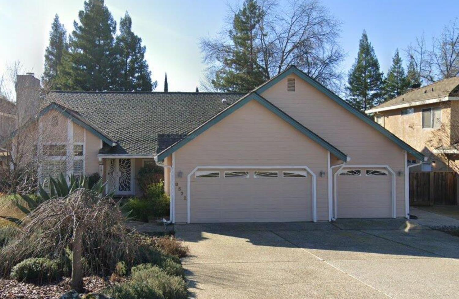 Home exterior with two garage doors, blue-green trim, and a broad driveway.
