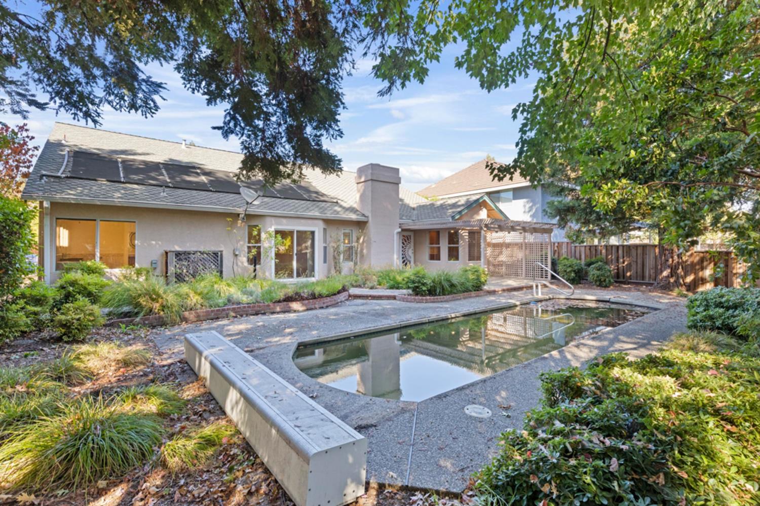 Single-story home behind a rectangular pool, surrounded by mature trees and landscaped gardens.
