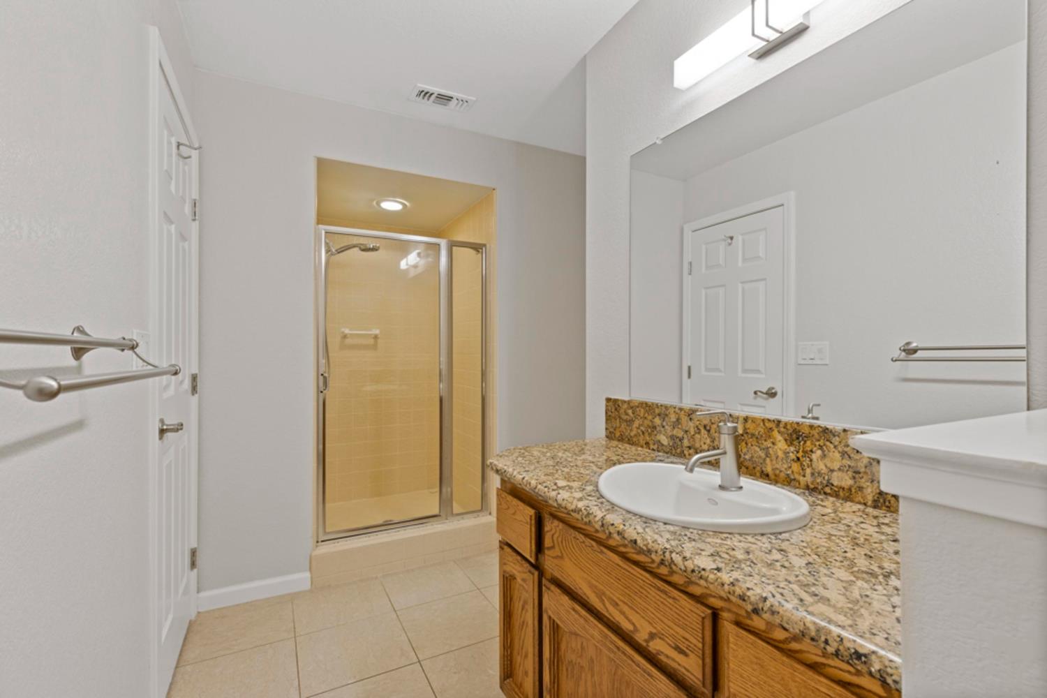 Bathroom with a glass shower and wood vanity topped with granite.
