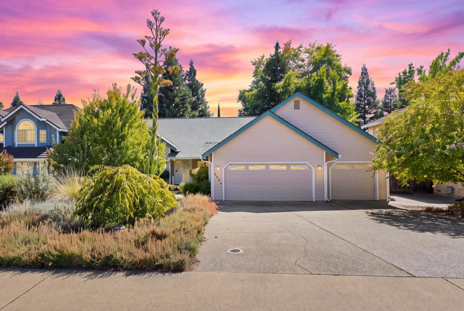 Suburban home with two garage doors, landscaped front yard, and vivid pink sunset sky.