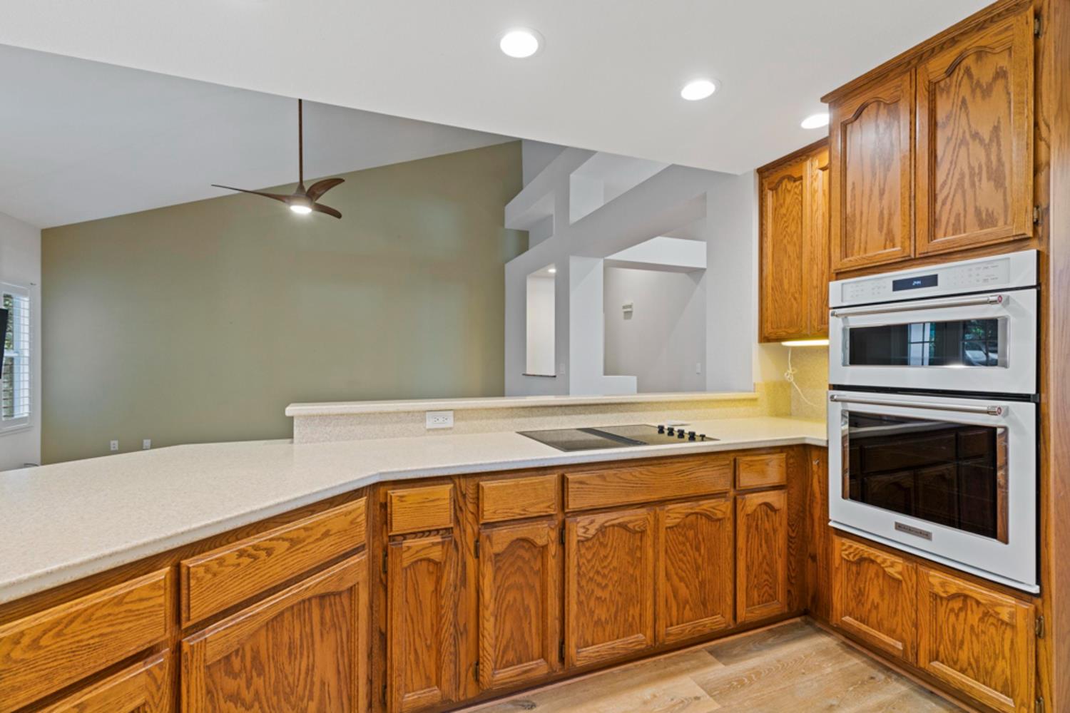 Kitchen with honey-toned wood cabinets, light countertops, and stacked white oven and microwave.
