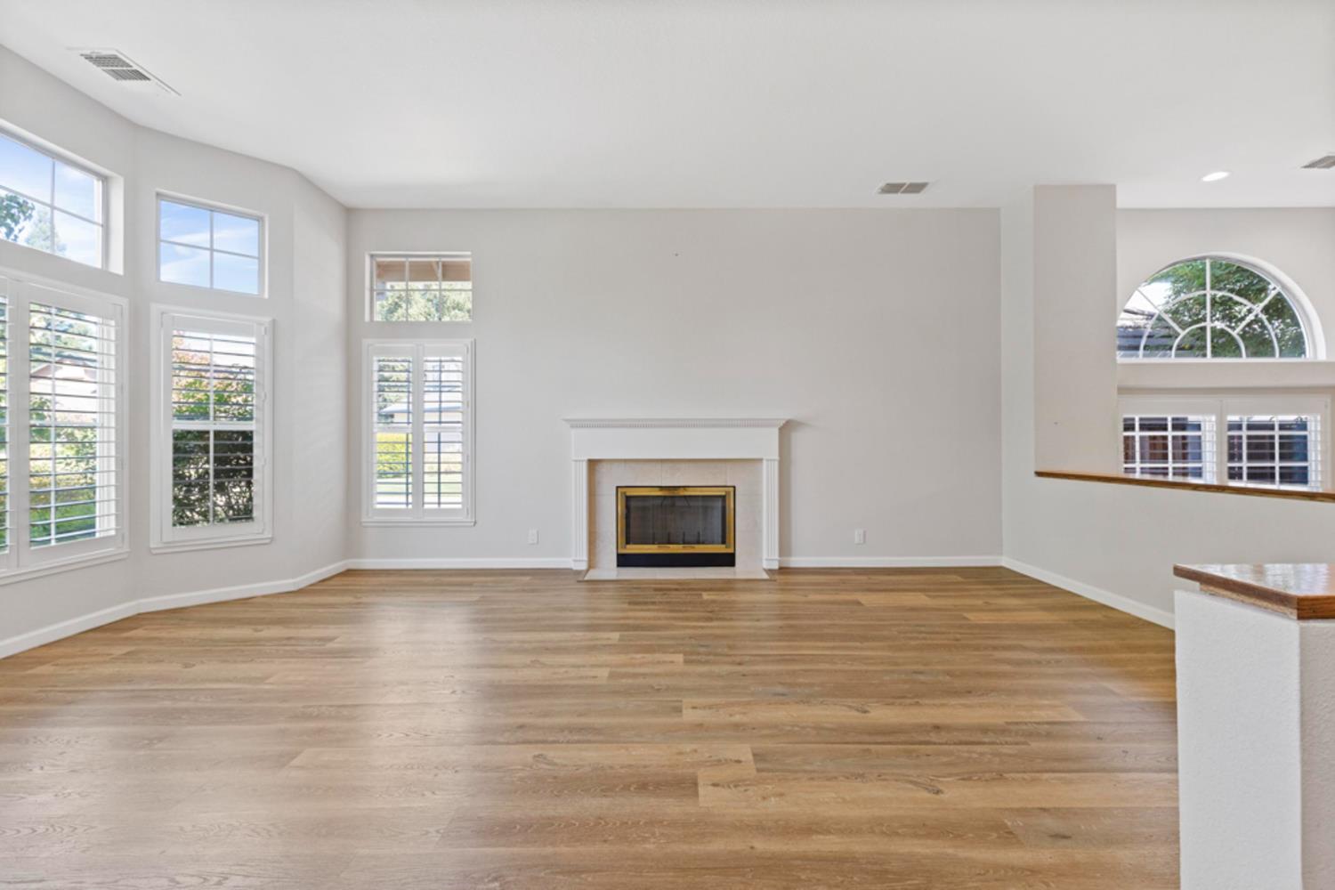 Empty living room with a fireplace, wood floors, and tall shuttered windows.
