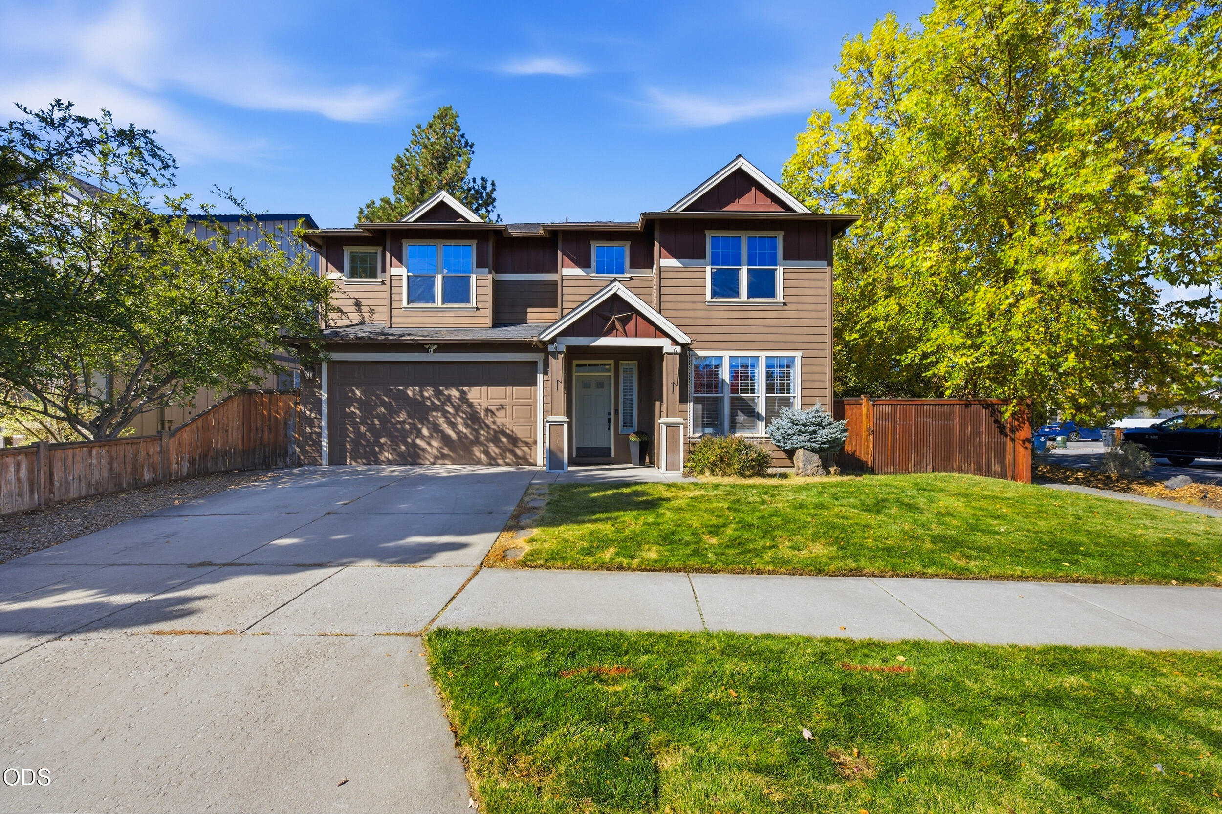 Two-story brown house with a double garage, covered entry, and leafy front yard.