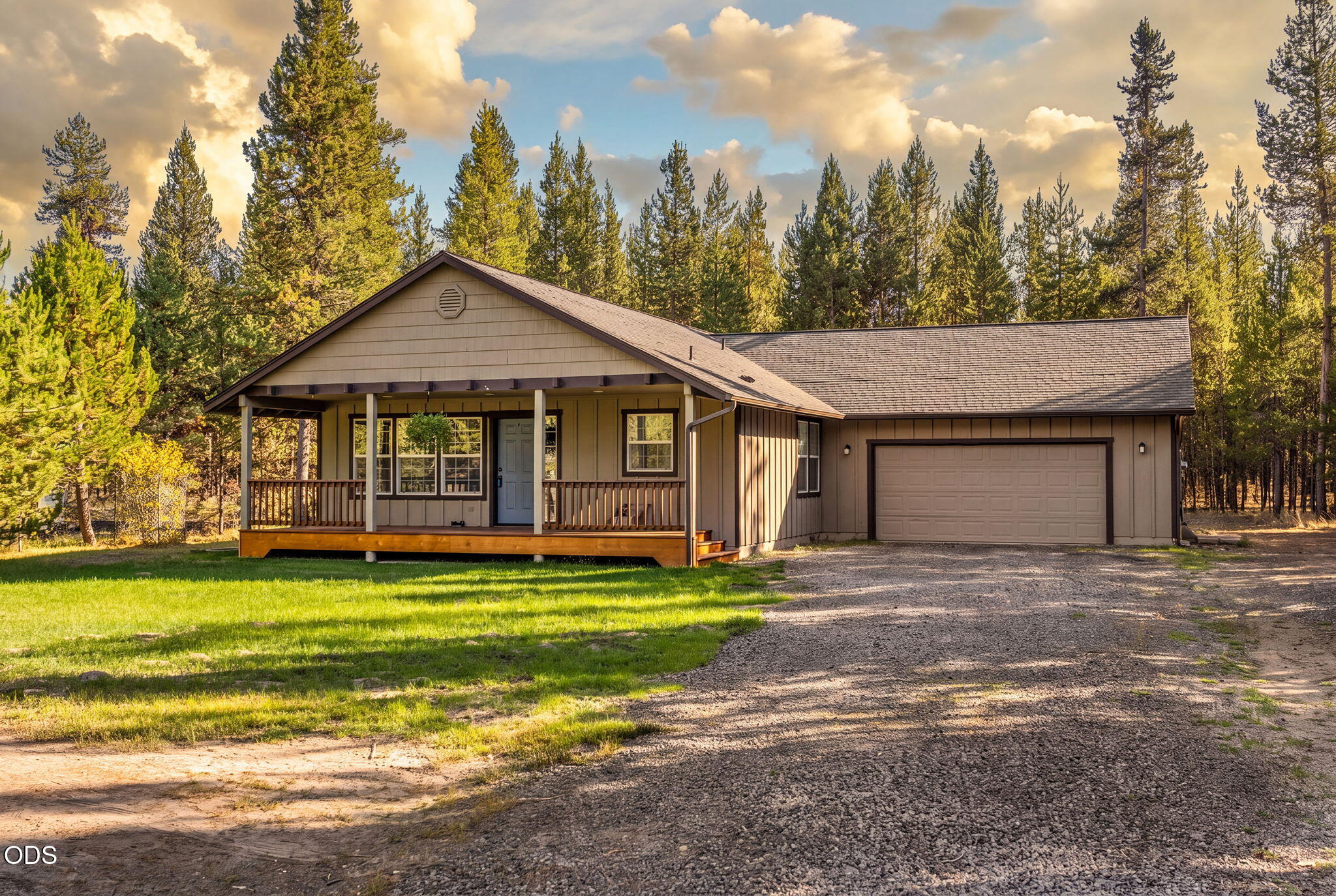 Single-story building with a covered porch and attached garage among pine trees.