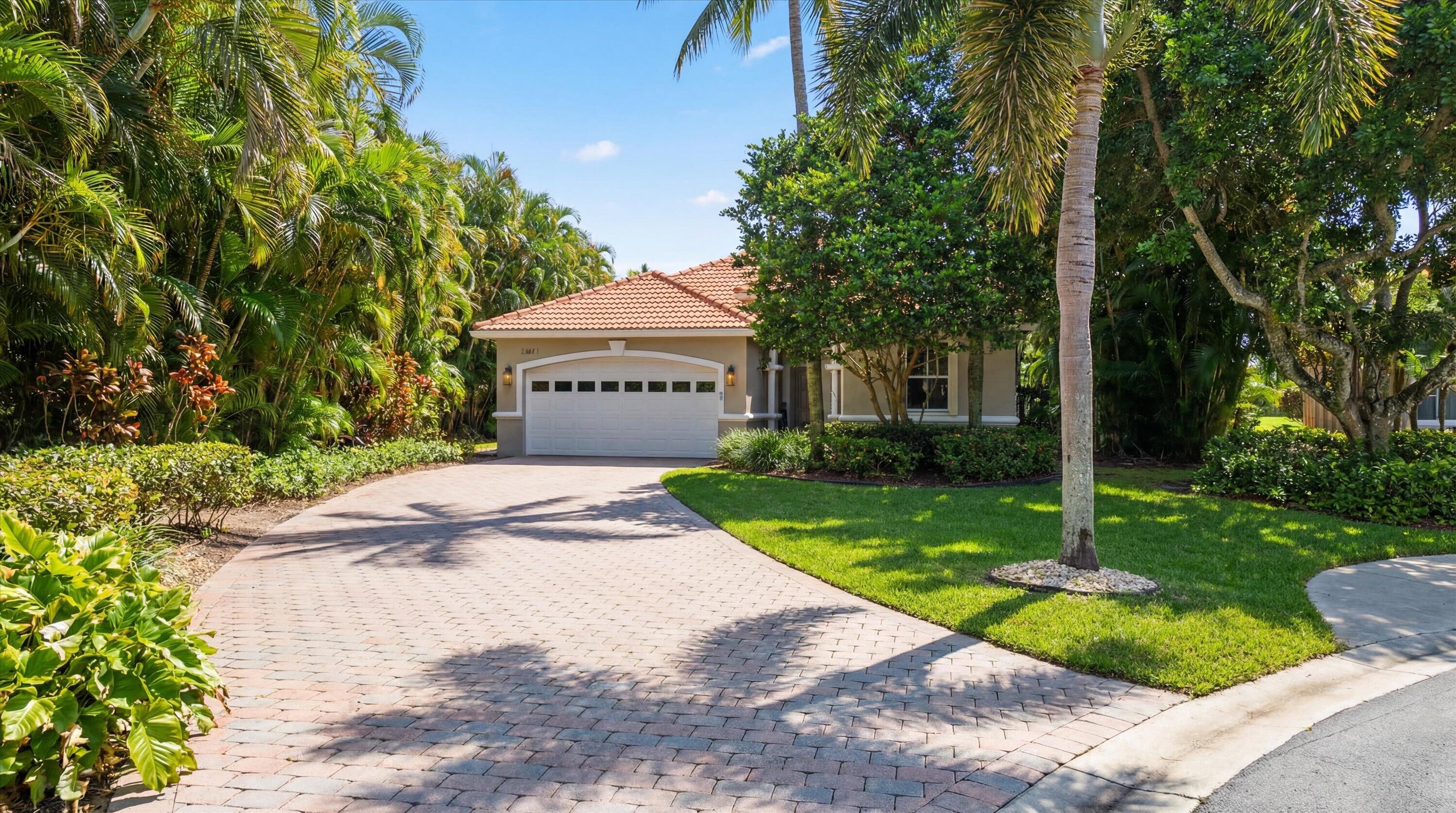 Single-story home with a terracotta tile roof, broad paved driveway, and lush palm landscaping.