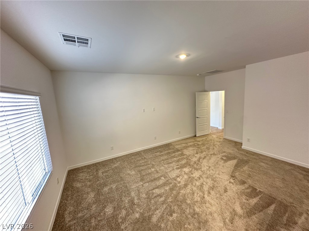Empty carpeted bedroom with window blinds and an open doorway.