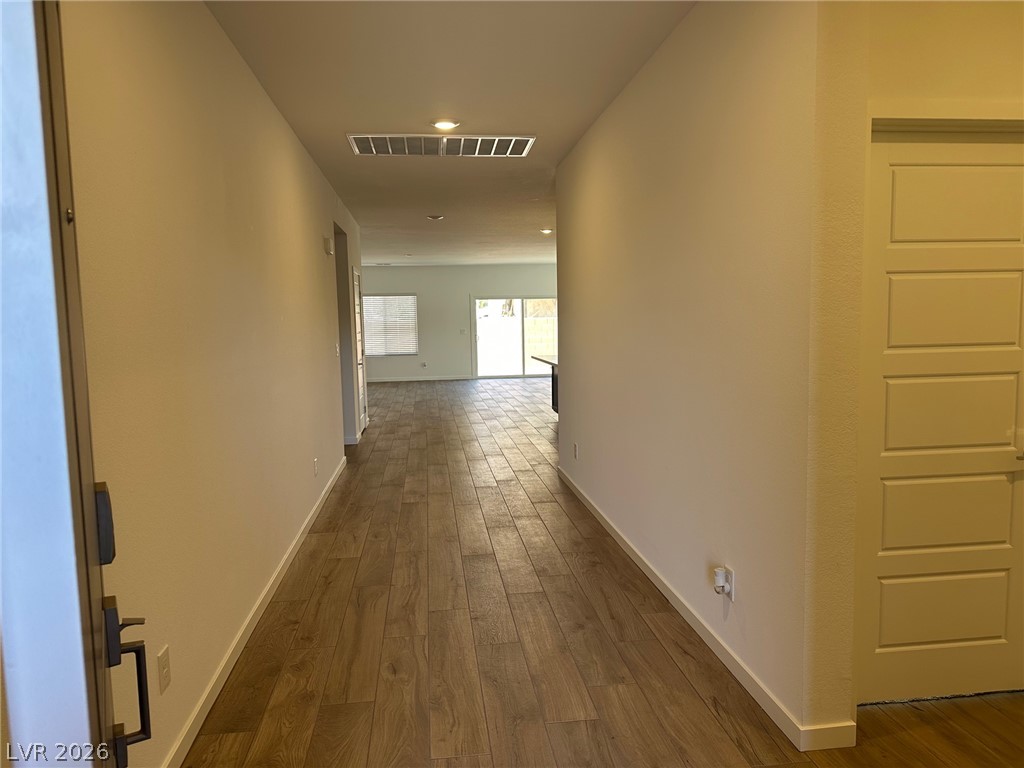 Empty hallway with wood-look tile flooring leading to a bright living area.