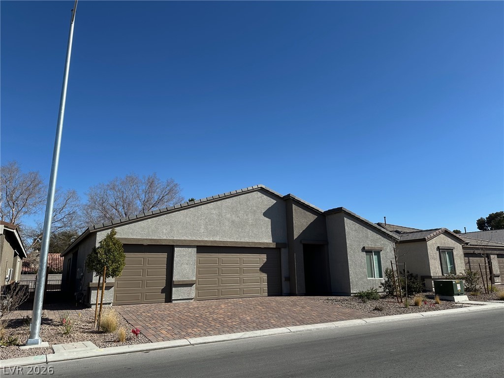 Gray single-story home with a two-car garage, brick-paver driveway, and desert landscaping.