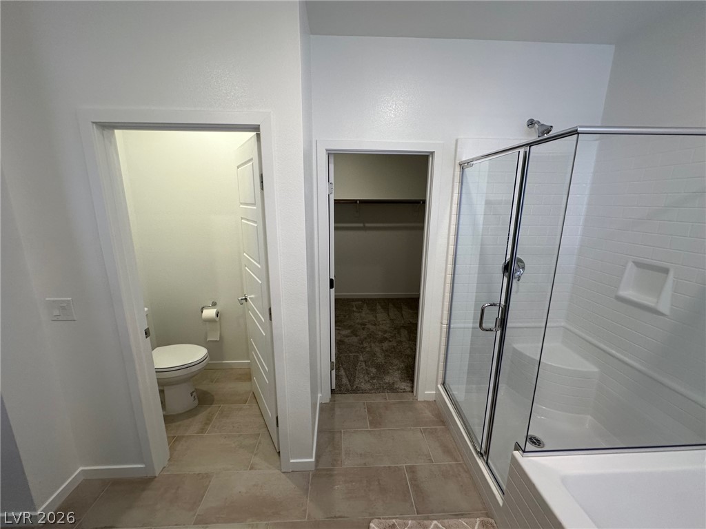 Bathroom with a glass-enclosed tiled shower and open doorways to a toilet room and closet.