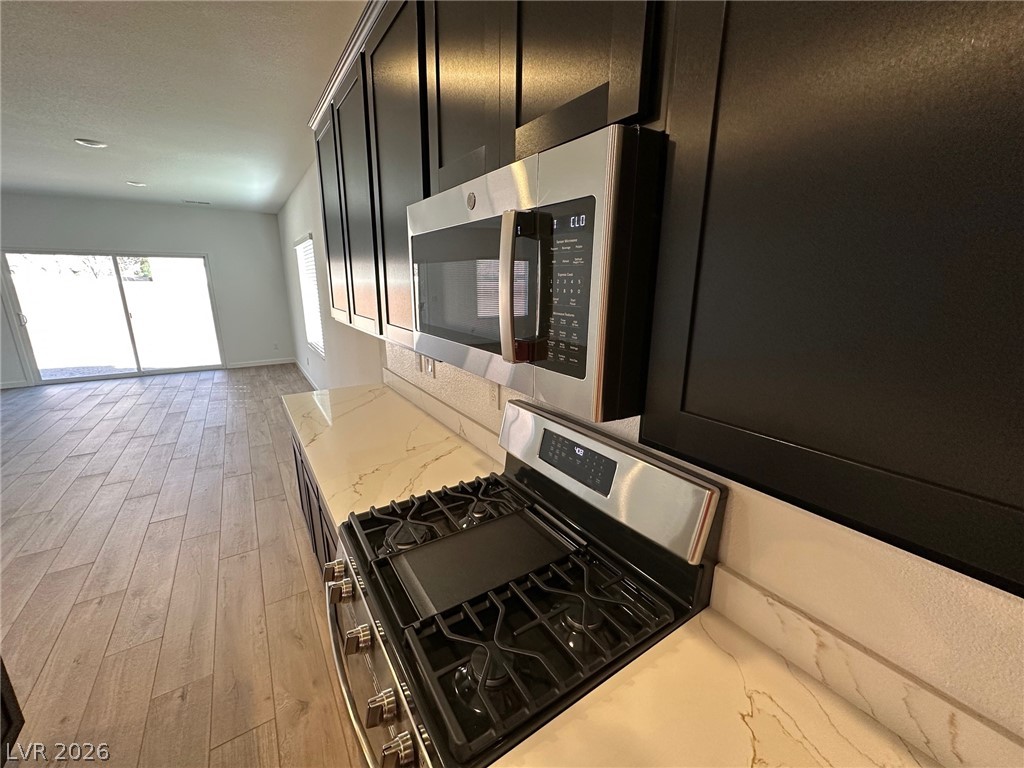 Vacant kitchen with dark cabinets, stainless appliances, gas range, and marble-look countertops.