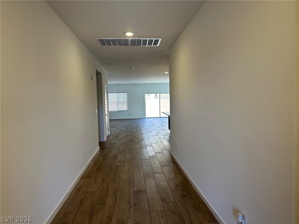 Empty hallway with wood-look flooring leading to a bright room with a sliding glass door.
