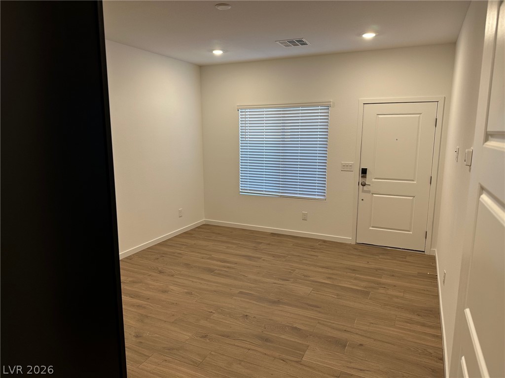 Empty room with wood-look flooring, closed window blinds, recessed lights, and a paneled entry door.