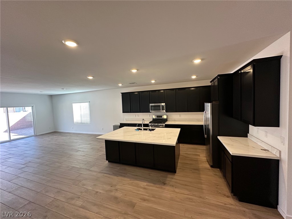 Open-plan kitchen with dark cabinets, a large white island, stainless steel appliances, and adjoining living area.