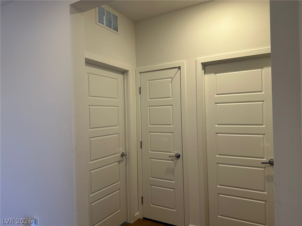 Hallway with three white paneled doors and a high wall vent.
