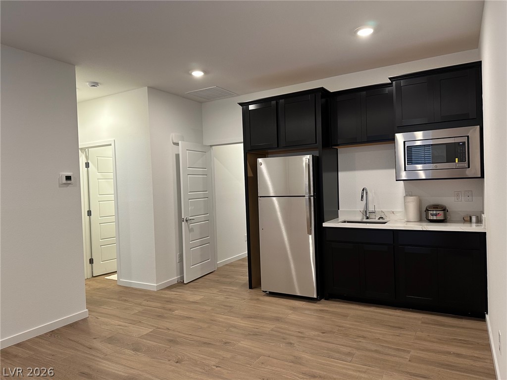 Kitchen with dark cabinets, stainless appliances, and wood-look flooring.