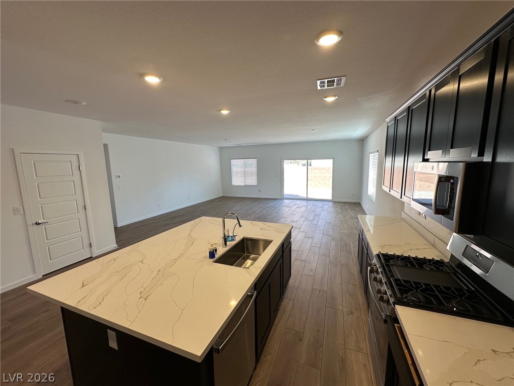 Unfurnished kitchen with a large stone-look island, dark cabinets, and stainless steel appliances opening to a living area.