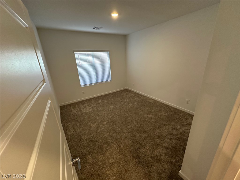 Empty bedroom with brown carpet and a window fitted with white blinds.