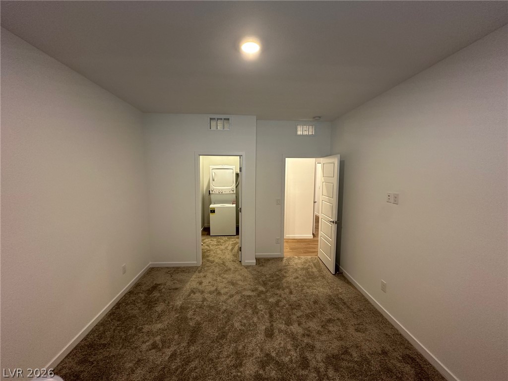 Empty carpeted room with a recessed light and doorways to a laundry area and hall.